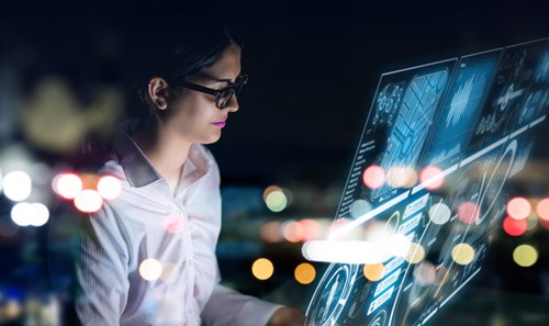 Woman in white shirt and black glasses sits behind a computer generated screen