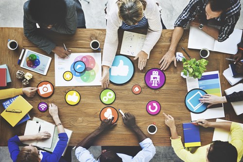 6 colleagues sit around a table filled with sheets, icons and tablets