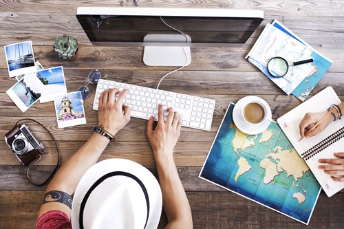 Aerial view of man sitting at computer surrounding by a camera, maps and photos