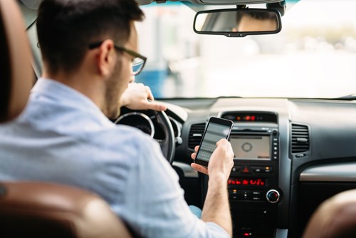 Man in a shirt at the wheel of a car looks at his mobile phone