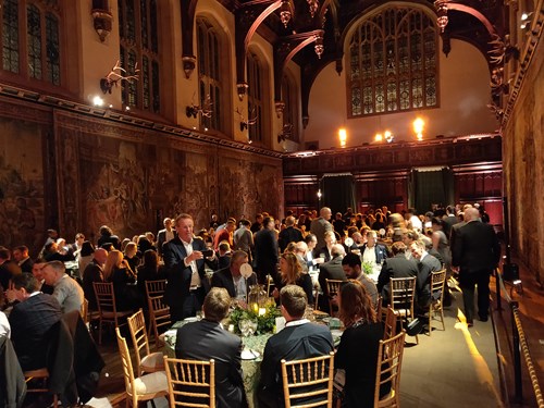 Dinner tables set in the great hall of Hampton Court Palace, a wood paneled, high-ceiling hall.