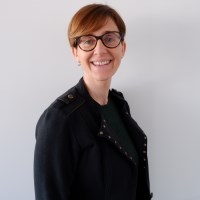 Head shot of a business woman wearing a black shirt and black rimmed glasses