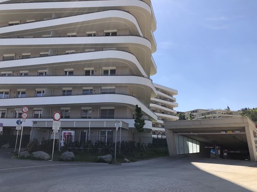 White multistory residential building with balconies and blue sky behind.