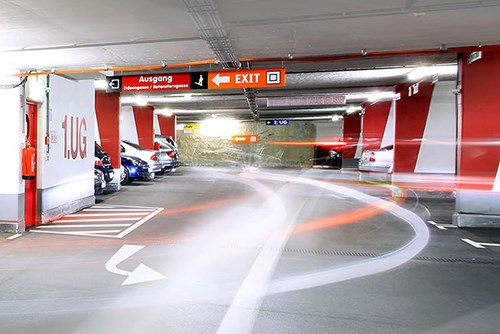 Inside a parking garage with red columns and an exit sign