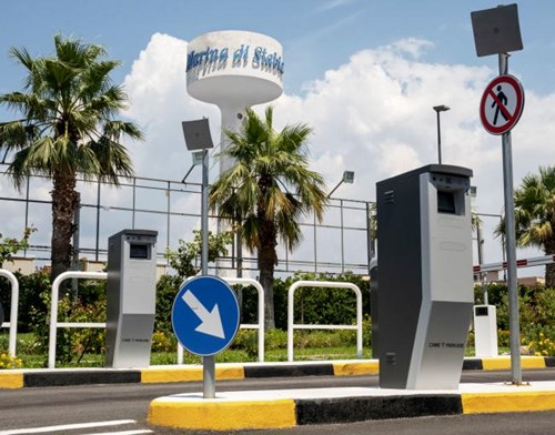 Entry and Exit lane of an outdoor parking lot, with palm trees, yellow and black chevron curb and payment machines