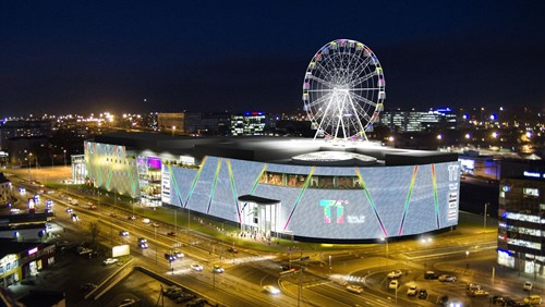 Night photograph of shopping center illuminated with ferris wheel on roof.