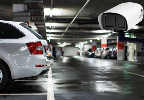 Back of a white car parked in a wet parking garage with a white LPR camera