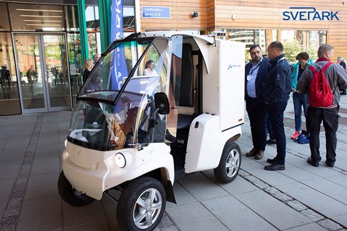 Small EV parked outside conference center with people passing by