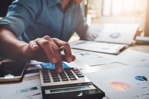 Man at a desk uses calculator and looks at papers filled with graphs