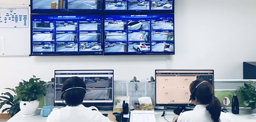 Wallmounted TV screens display CCTV footage from several cameras, and two people look at computer screens.