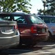 Three cars parked in a lot with trees and red brick house in background