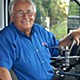 Smiling gray-haired man in blue shirt sitting in driver seat of a bus