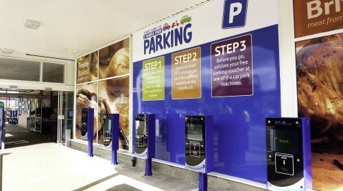 parking machines and an explanation billboard next to entrance of a supermarket