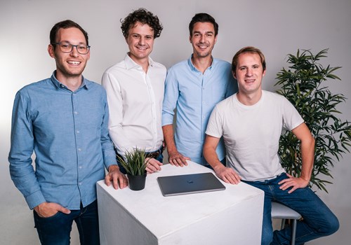 Four men sit around a white cube table, with a plant on the table and behind them