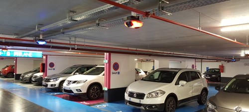 Parking garage with blue walkway and blue disabled parking displays. Parking guidance sensors from the ceiling illuminate red and blue and white and silver cars are parked in the bays.