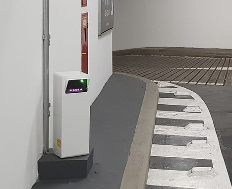 A camera displaying green and purple lights in a white box at the entry lane of a parking garage