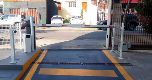 Parking barrier at a parking lot, with a street in the background and two white parked cars.