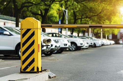 Yellow parking barrier equipped with an LPR camera, a row of white cars in the parking lot behind