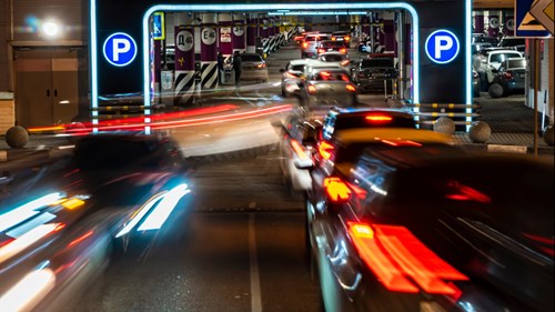 Night time photo of cars opening a parking garage with red and white headlights