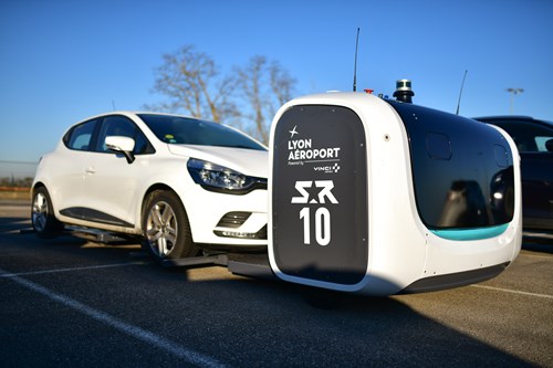 An automated parking robot lifting a white car in an outdoor parking lot