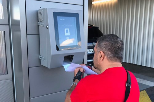 Male wheelchair user interacts with screen to drop off his car at parking garage