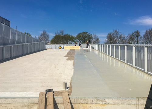 Parking ramp under construction, leading to the rooftop, blue sky, trees and workmen in the background