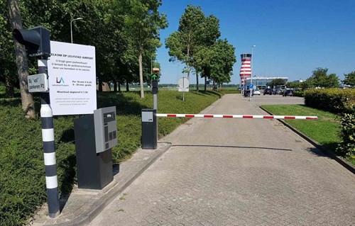 Red and white parking barrier with a sign and a red and white striped airport tower in the background