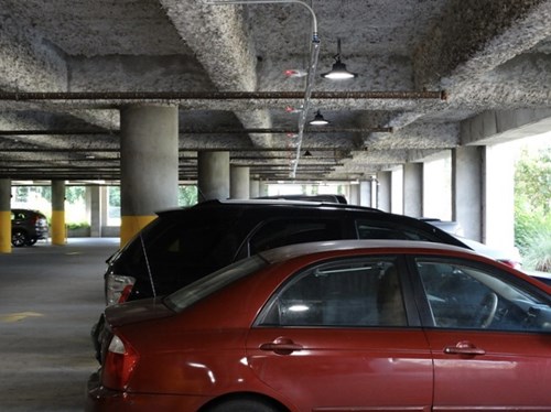 Red and black car parked in a multistory car park, trees in background through windows