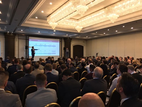 Man presents to audience, large screen behind him